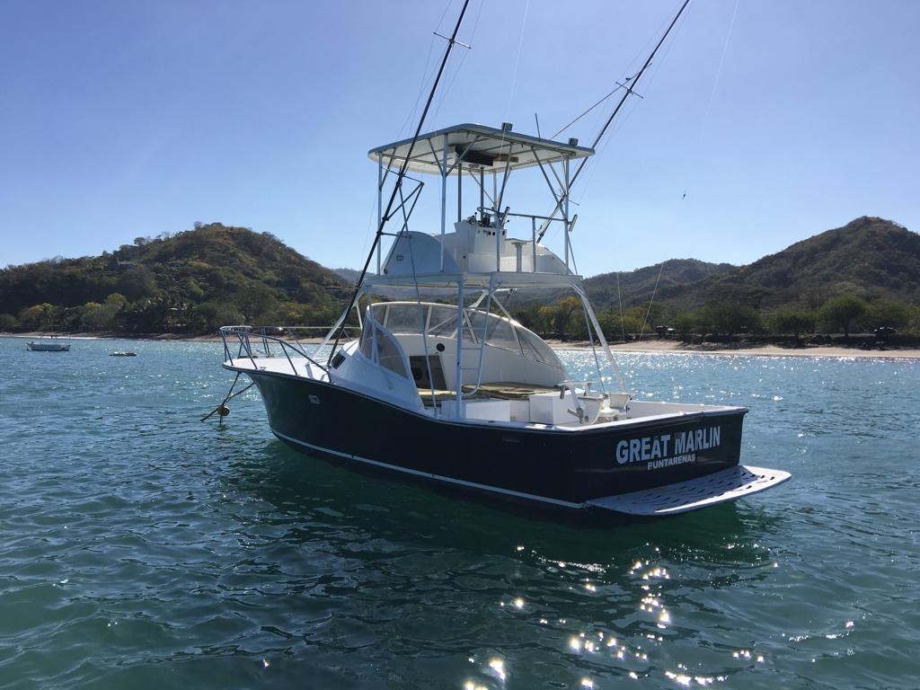 Great Marlin at anchor off Herradura Bay seen from astern: black hull, open fighting cockpit, white tuna tower and outriggers, the name and PUNTARENAS lettered across the transom