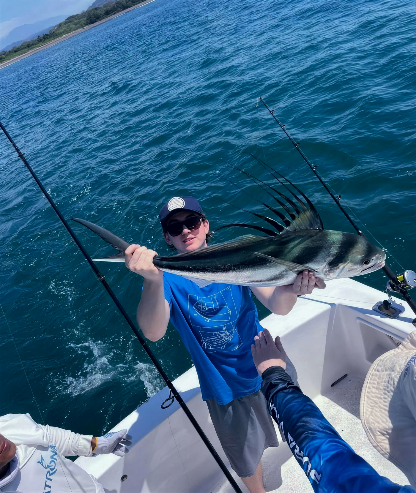 A roosterfish held up on the bow before release, the coast behind